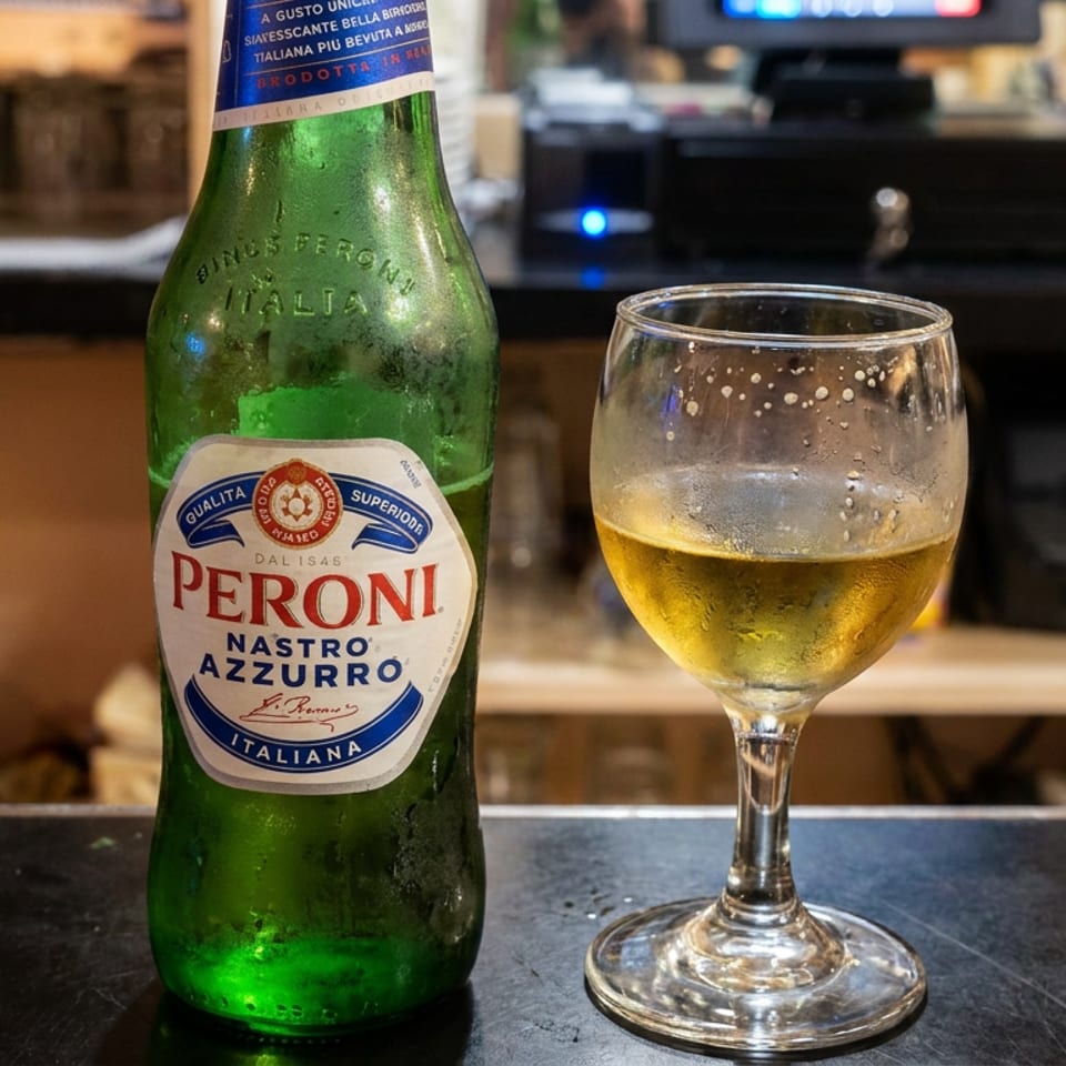 Peroni Nastro Azzurro beer bottle beside a filled beer glass on a restaurant bar.