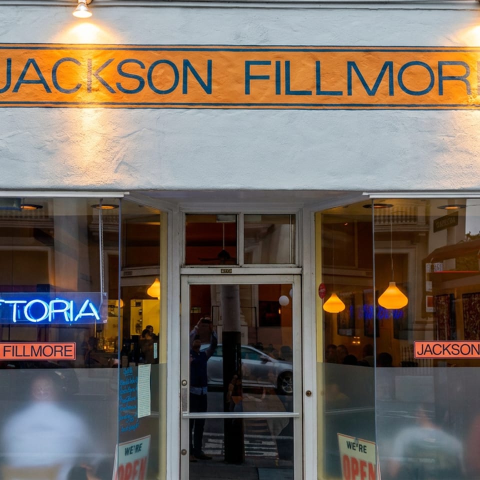 Jackson Fillmore trattoria restaurant storefront with illuminated signage, glowing interior lights, and open signs in the windows.