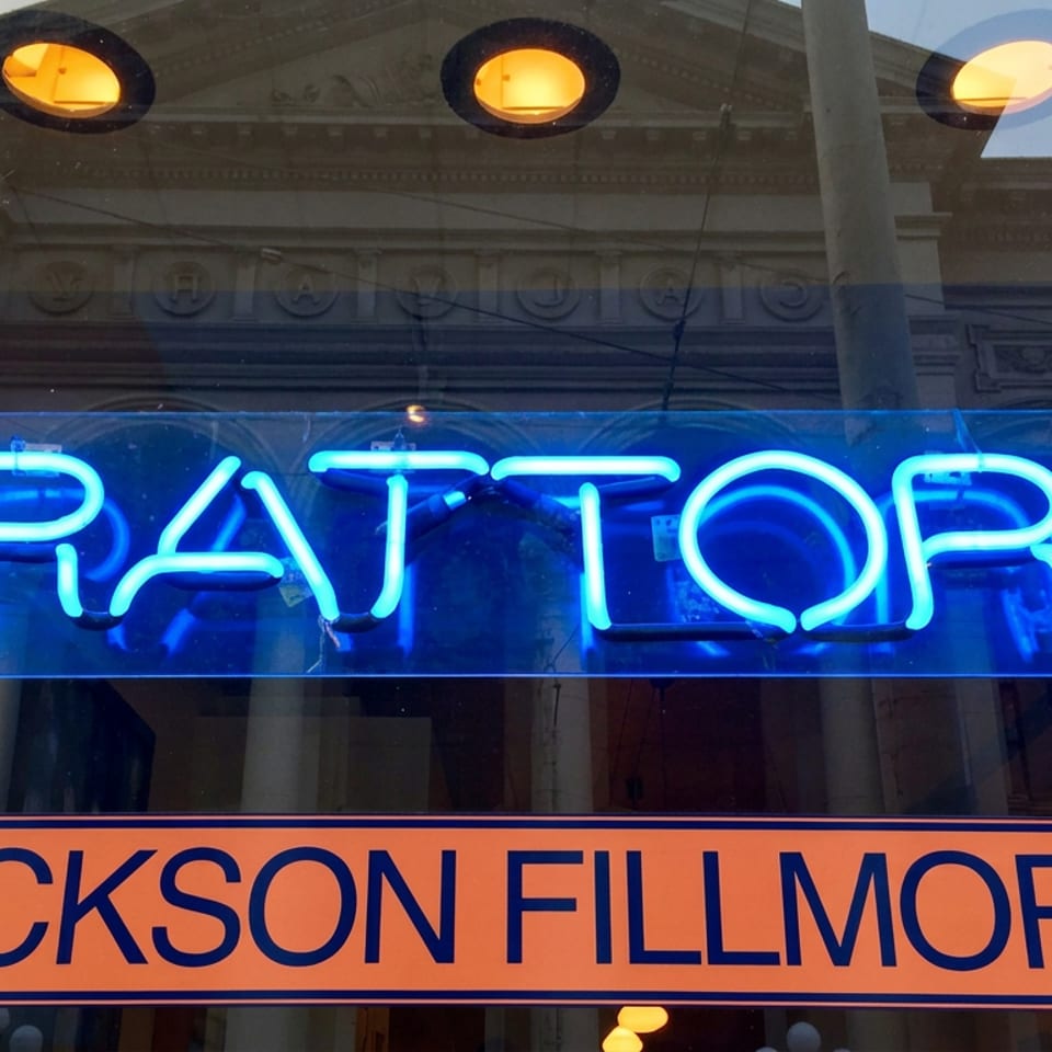 Neon blue Trattoria sign above an orange Jackson Fillmore street sign, reflected in a restaurant window.